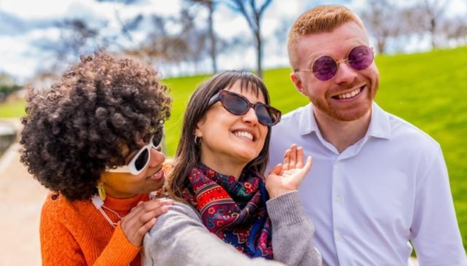 Three adults wearing sunglasses and smiling outdoors